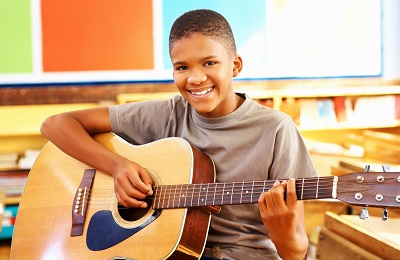 child with a smile holding a
        guitar